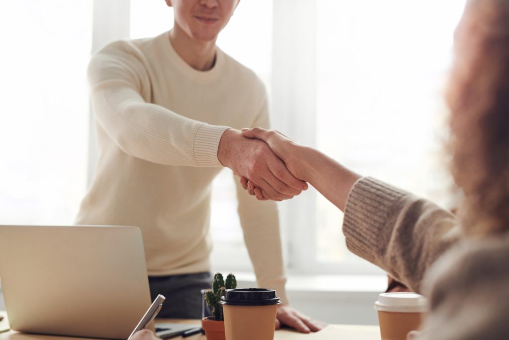 Two people shaking hands at a desk in an office environment.